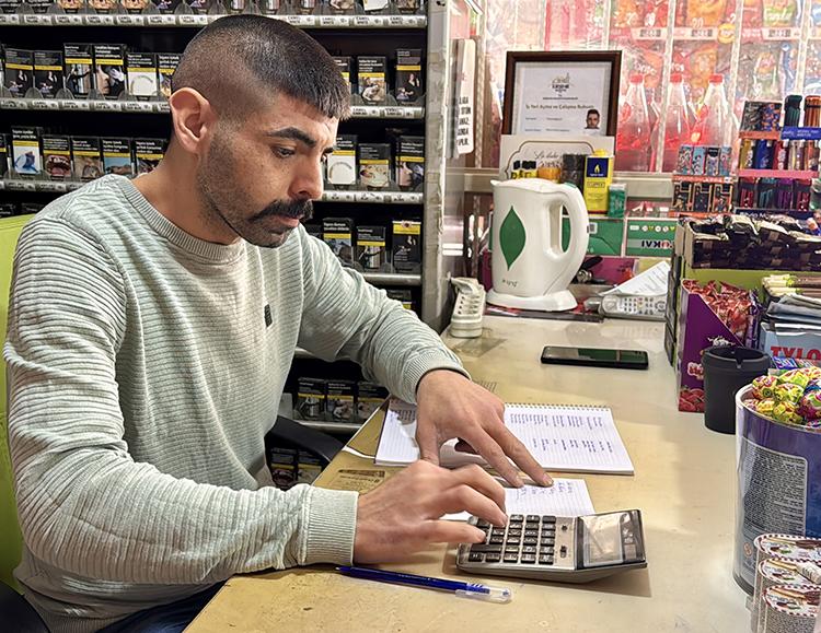 Dono de conveniência fazendo contas no caderno com calculadora
